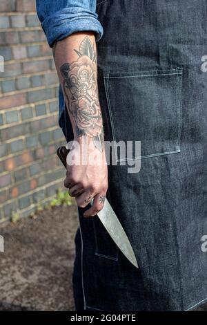 Mann mit Tattoo auf der Hand hält Messer Stockfoto