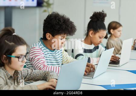 Verschiedene kleine Kinder, die Laptops benutzen, während sie sitzen Rudern im IT-Klassenzimmer Stockfoto