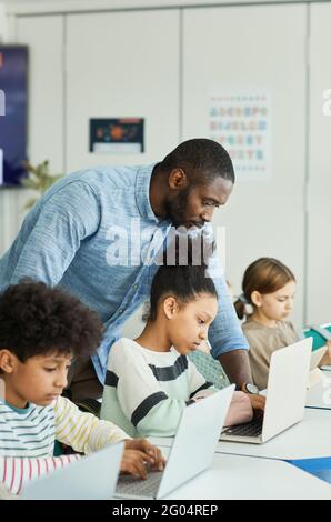 Seitenansicht Porträt eines männlichen Lehrers, der Kindern beim Umgang mit Computern hilft In DER IT-Klasse Stockfoto