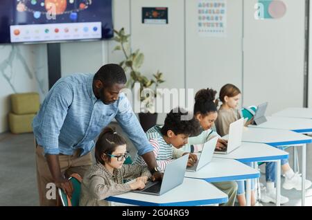 Seitenansicht Porträt eines männlichen Lehrers, der Kindern bei der Nutzung von Computern in der IT-Klasse hilft, Platz kopieren Stockfoto
