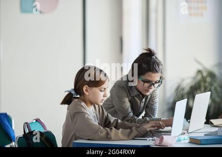 Seitenansicht Porträt von zwei Kindern, die Computer in minimalem Schulinnenraum benutzen, Kopierraum Stockfoto