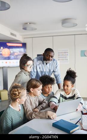 Vertikale Aufnahme einer Gruppe von Kindern, die zusammen einen Laptop benutzen Am Tisch in der modernen Schule Stockfoto