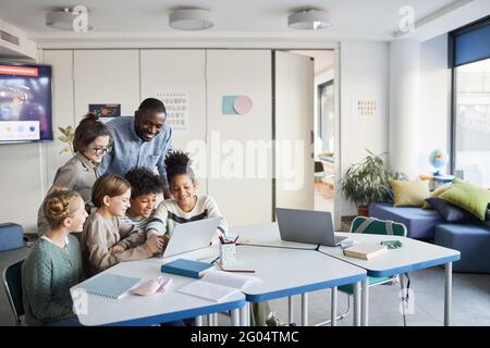 Verschiedene Gruppe von Kindern mit männlichen Lehrer mit Laptop zusammen in der modernen Schule Klassenzimmer, Copy Space Stockfoto