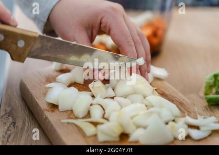 Seitenansicht auf Händen einer unbekannten Frau mit Messer an Brett in der Küche schneiden Stücke von Zwiebel für die Vegane oder vegetarische Suppe Kochen gesunde Mahlzeit f Stockfoto