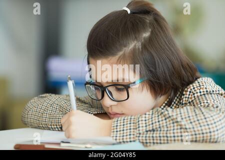 Nahaufnahme Porträt von niedlichen Jungen trägt Brille sitzen an Schreibtisch in der Schule Klassenzimmer und Schreiben Stockfoto