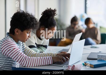 Seitenansicht Porträt von zwei Kindern, die Computer in modernen Schulklassen benutzen, Kopierraum Stockfoto