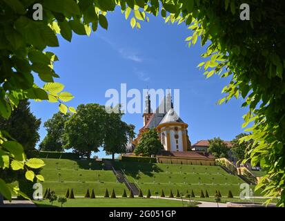 31. Mai 2021, Brandenburg, Neuzelle: Blick vom Klostergarten auf die katholische Kirche. Im Klostergarten Neuzelle in der oder-Spree wird seit über einem Jahr an der dritten und letzten Bauphase zur Sanierung des Barockgeländes gearbeitet. Zuvor waren in diesem Gebiet die Lauben eines Schelfgartens aus DDR-Zeiten abgerissen worden. Bis 2022 soll hier eine Baumschule mit Gewächshaus, Küchengarten und Kräutergarten sowie symmetrisch angelegte Blumenbeete, die von Hecken und Obstbäumen umrahmt werden, errichtet werden. Seit 1998 wird an der Gartenanlage gearbeitet, die Stockfoto