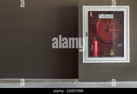 Ein weißer Feuerwehreinbauschrank oder ein Feuerlöschschrank mit Brandschutz an einer braunen Betonwand auf dem Parkplatz. Notfeuer Ext Stockfoto