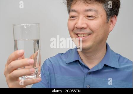 Asiatischer Mann mittleren Alters mit einem Glas Wasser. Stockfoto