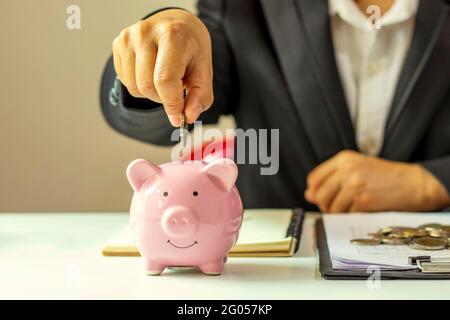 Einsparungs- und Finanzierungsideen. Geschäftsleute legen Geldmünzen in ein Sparschwein, um Geld zu sparen und ihre Finanzen zu planen. Stockfoto