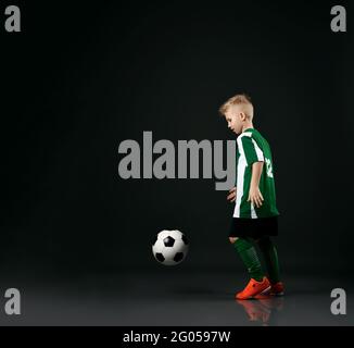Blonde junge Kind in Sport grün und weiß Kleidung laufen Und mit Fußball spielen Stockfoto