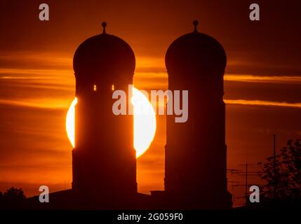 München, Deutschland. Juni 2021. Die Sonne geht am frühen Morgen zwischen den zwei 99 Meter hohen Türmen der Frauenkirche auf, die im Herzen der bayerischen Hauptstadt steht. Das Bild wurde mit einem 1050 Millimeter Teleobjektiv der Theresienwiese aufgenommen. Kredit: Peter Kneffel/dpa/Alamy Live Nachrichten Stockfoto