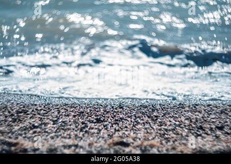 Abstrakte Natur Sommer oder Frühling Meer Meer Hintergrund. Kleine Wellen auf der goldenen, warmen Wasseroberfläche verwischen sich in Bewegung mit Bokeh-Lichtern vom Sonnenuntergang. Urlaub Stockfoto