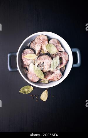 Scheiben leicht gesalzener Makrelenfische mit Piment und Lorbeerblatt auf einem schwarzen Holztisch. Marinierte Makrelen mit Gewürzen salzen. Stockfoto