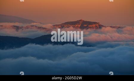 Sonnenuntergang und Alpenglow über dem Berg La Mola, mit niedrigen Wolken, vom Berg Montserrat aus gesehen (Barcelona, Katalonien, Spanien) Stockfoto