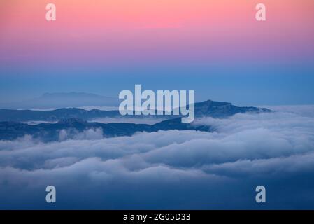 Sonnenuntergang und Alpenglow über dem Berg La Mola, mit niedrigen Wolken, vom Berg Montserrat aus gesehen (Barcelona, Katalonien, Spanien) Stockfoto