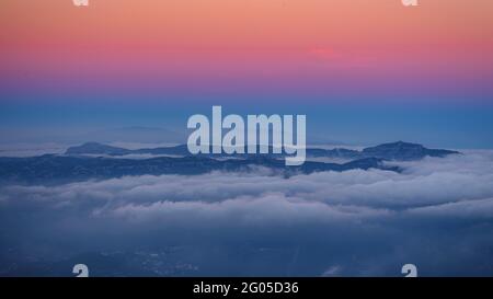 Sonnenuntergang und Alpenglow über dem Berg La Mola, mit niedrigen Wolken, vom Berg Montserrat aus gesehen (Barcelona, Katalonien, Spanien) Stockfoto