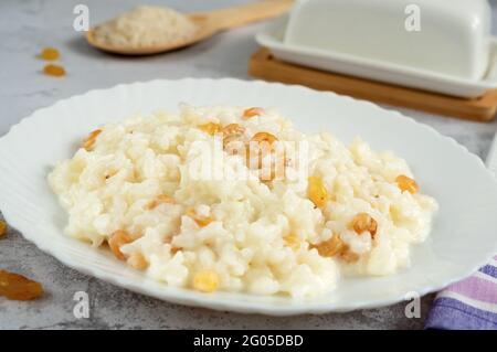 Köstlicher Reisbrei mit Rosinen in einer Schüssel auf einem grauen Tisch, Seitenansicht Stockfoto