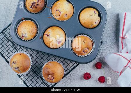 Gebackene Himbeer-Muffins auf einem Kühlgestell auf blauem Beton-Tischhintergrund. Frühstückskonzept Stockfoto