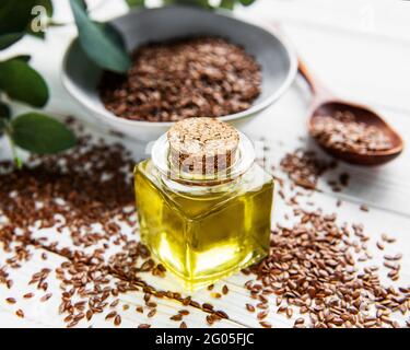 Leinsamen oder Leinsamen in Löffel und Schüssel mit Glas Leinöl auf Holzkulisse Stockfoto