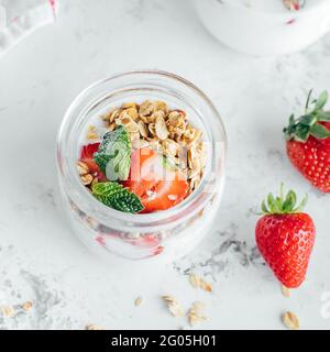 Frühstücksangebot. Glas mit leckeren Parfaits aus Müsli, Erdbeeren und Joghurt auf Marmortisch Stockfoto