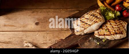 Hoher Winkel von geröstetem Fischfilet, serviert mit Gemüse auf Holzbrett auf dem Tisch Stockfoto