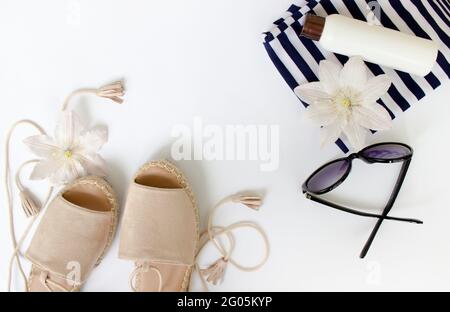 Sommer flach Lay. Sommersandalen, weiße Blumen, Sonnenbrillen und eine weiße Flasche.Draufsicht. Kreativer Hintergrund. Stockfoto