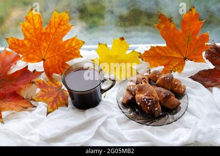 Eine Tasse Kaffee Cappuccino, Croissant und Herbstblätter bleiben auf der Fensterbank. Herbstdekor, Herbststimmung, Stillleben im Herbst Stockfoto