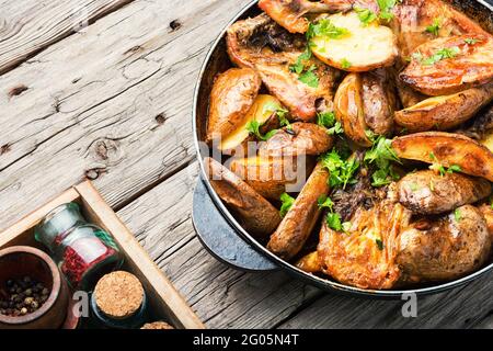 Hähnchenfleisch mit Kartoffeln in einer Pfanne gebraten.Hähnchenstücke gebacken Mit Gemüse auf rustikalem Holzhintergrund Stockfoto