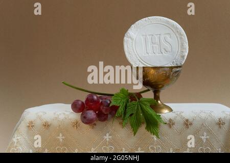 Das Konzept des Fronleichnamsfestes. Heilige Kommunion und Tasse Glas mit Rotwein auf dem Tisch. Stockfoto