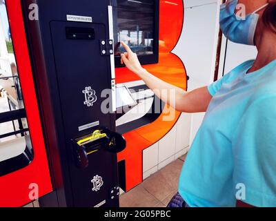 Geldautomat mit Bitcoin. Frau in medizinischen Maske Kauf Bitcoins. Kryptowährung. Geldtechnologie Stockfoto