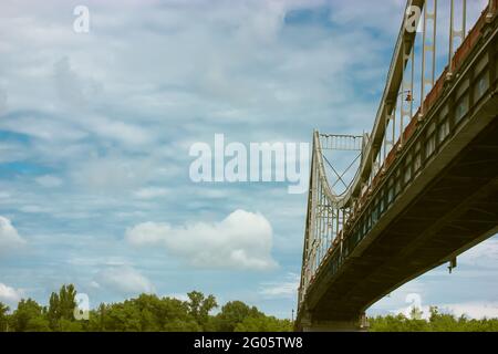 Eine moderne Fußgängerbrücke aus Eisen mit Kabelgefüge und einer Laterne vor einem blau bewölkten Himmel am Sommertag. Blick von unten auf einen Hig Stockfoto