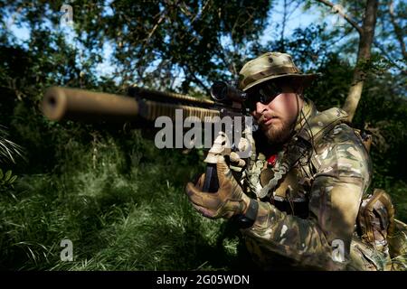 Airsoft-Spieler in Tarnuniform, der auf den Anblick der Waffe zielt Stockfoto