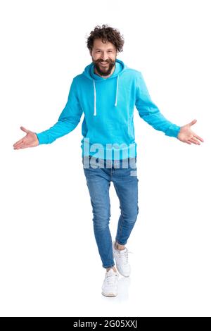 Enthusiastischer bärtiger Mann mit blauem Kapuzenpullover, der die Arme öffnet, umarmt und präsentiert, während er selbstbewusst lächelt und isoliert auf weißem Hintergrund in s läuft Stockfoto