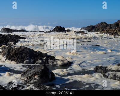 Schaumiges, schaumiges Wasser in der Brandung, das nach rauem Wind durch die Felsen auf den Strand spült Stockfoto