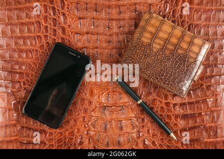 Telefon, Brieftasche und Stift liegen auf brauner Krokodilhaut. Unternehmen. Draufsicht Stockfoto