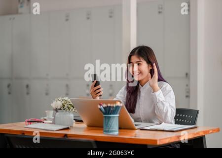 Glückliche junge asiatische Frau hält Telefon Blick auf den Bildschirm winkende Hand Video Anruf Distanz Freund online in mobilen Chat-App mit Smartphone-Videochat Stockfoto