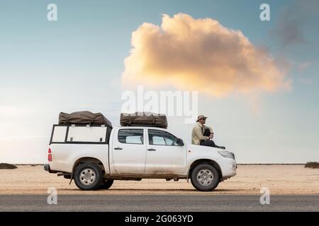 Ein Tourist sitzt in seinem SUV mit Zelten auf einer Straße in der namibischen Wüste in Afrika. Safari-Expedition und Reise-Abenteuer-Konzept Stockfoto