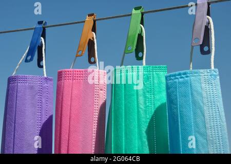 Seitenansicht der mehrfarbigen chirurgischen Gesichtsmaske (Einweg-Maske), die auf Wäscheleinen mit Wäscheklammer hängt, Konzept zum Schutz der Umwelt vor Abfall und Verschmutzung. Stockfoto