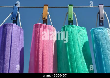 Vorderansicht der mehrfarbigen chirurgischen Gesichtsmaske (Einweg-Maske) hängt auf Wäscheleine Draht mit Wäscheklammer, Konzept zum Schutz der Umwelt vor Abfall und Verschmutzung. Stockfoto