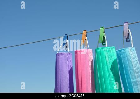 Konzept zum Schutz der Umwelt vor Abfall und Verschmutzung mit negativem Raum, Foto von mehrfarbigen chirurgischen Gesichtsmaske (Einweg-Maske) hängen auf Wäscheleine Draht mit Wäscheklammer. Stockfoto