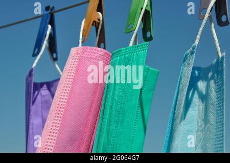 Seitenansicht der mehrfarbigen chirurgischen Gesichtsmaske (Einweg-Maske), die auf Wäscheleinen mit Wäscheklammer hängt, Konzept zum Schutz der Umwelt vor Abfall und Verschmutzung. Stockfoto