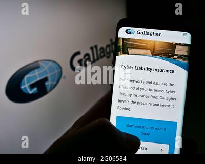 Person, die Mobiltelefon mit der Webseite der US-Versicherungsgesellschaft Arthur J. Gallagher Co. Auf dem Bildschirm vor dem Logo hält. Konzentrieren Sie sich auf die Mitte des Telefondisplays. Stockfoto