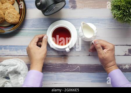 Draufsicht auf die Hand des Mannes, der Teetasse und einen Krug Milch hält Stockfoto