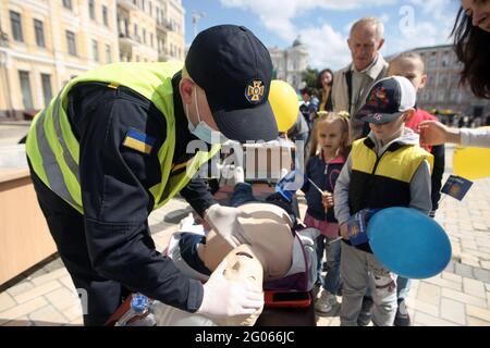 KIEW, UKRAINE - 1. JUNI 2021 - EIN Polizeibeamter zeigt Kindern erste-Hilfe-Grundlagen während der Feier des Internationalen Kindertages in Sofiiska S Stockfoto