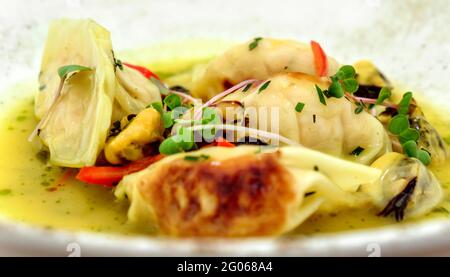 Knödel Gyoza mit Krabbenfüllung, serviert mit Muscheln und Mikrogemüse im Restaurant Stockfoto