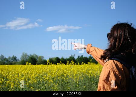 Das Mädchen in der Brille zeigt mit der Hand auf die Blumen. Reisen Sie außerhalb der Stadt. Sonniges Wetter. Wiese mit Blumen Stockfoto