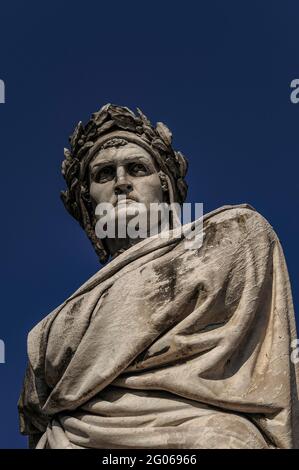 Dante Alighieri (c. 1265-1321), Dichter, Philosoph und Autor der Göttlichen Komödie, starrt in einen klaren blauen Himmel über der Franziskanerkirche Santa Croce aus dem 13. Jahrhundert auf der Piazza Santa Croce in Florenz, Toskana Italien. Das Denkmal, das Enrico Pazzi anlässlich des 600. Geburtstages von Dante in Florenz geschaffen hat, wurde 1865 in der Mitte des Platzes installiert, aber nach den verheerenden Überschwemmungen des Arno im Jahr 1966 an seinen heutigen Standort neben der Kirche verlegt. Stockfoto