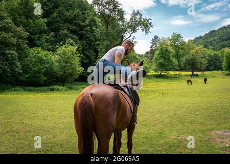 Ein junger Mann mit blauen Jeans, einem gemusterten Hemd und einem Cowboyhut, der auf sein Pferd klettert Stockfoto