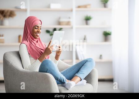 Junge Schwarze Muslimische Frau In Hijab Entspannung Im Stuhl Mit Digitalem Tablet Stockfoto
